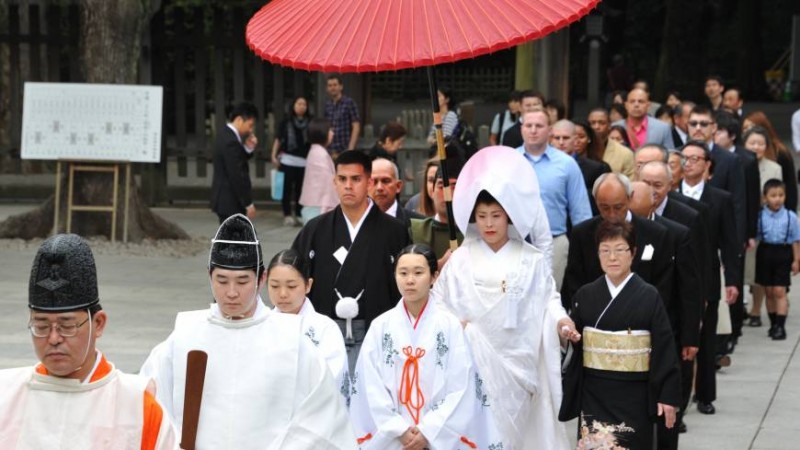 Jonathan Madrid, 24, and Nao Sasaki, 30, are led by priests to the wedding hall at Tokyo's Meiji Jingu on Saturday. | YOSHIAKI MIURA